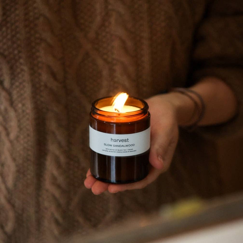 Hands holding lit Harvest Slow Sandalwood candle in amber jar