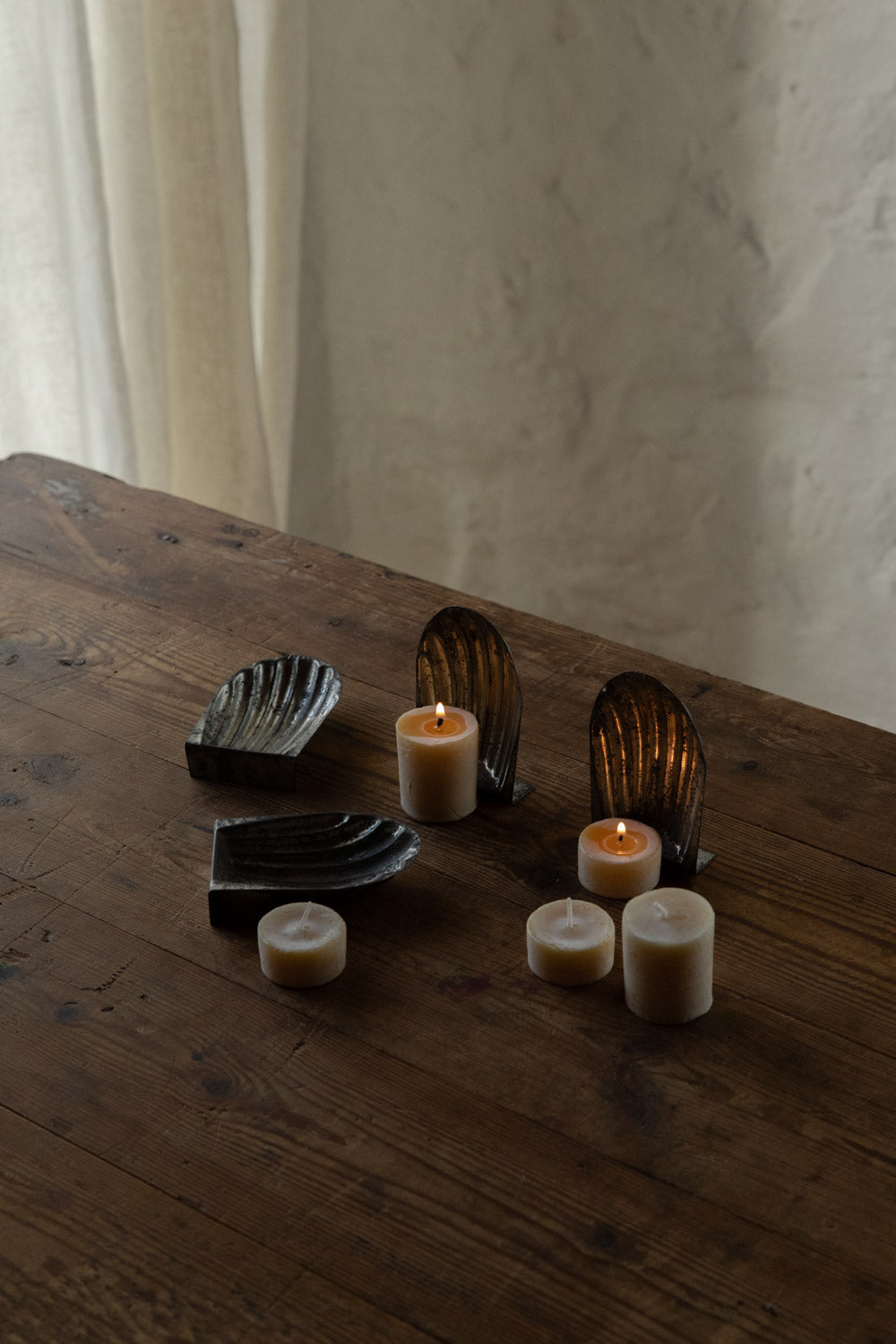 Decorative metal moulds stand against english beeswax tealight candles on a wooden surface with a neutral background.