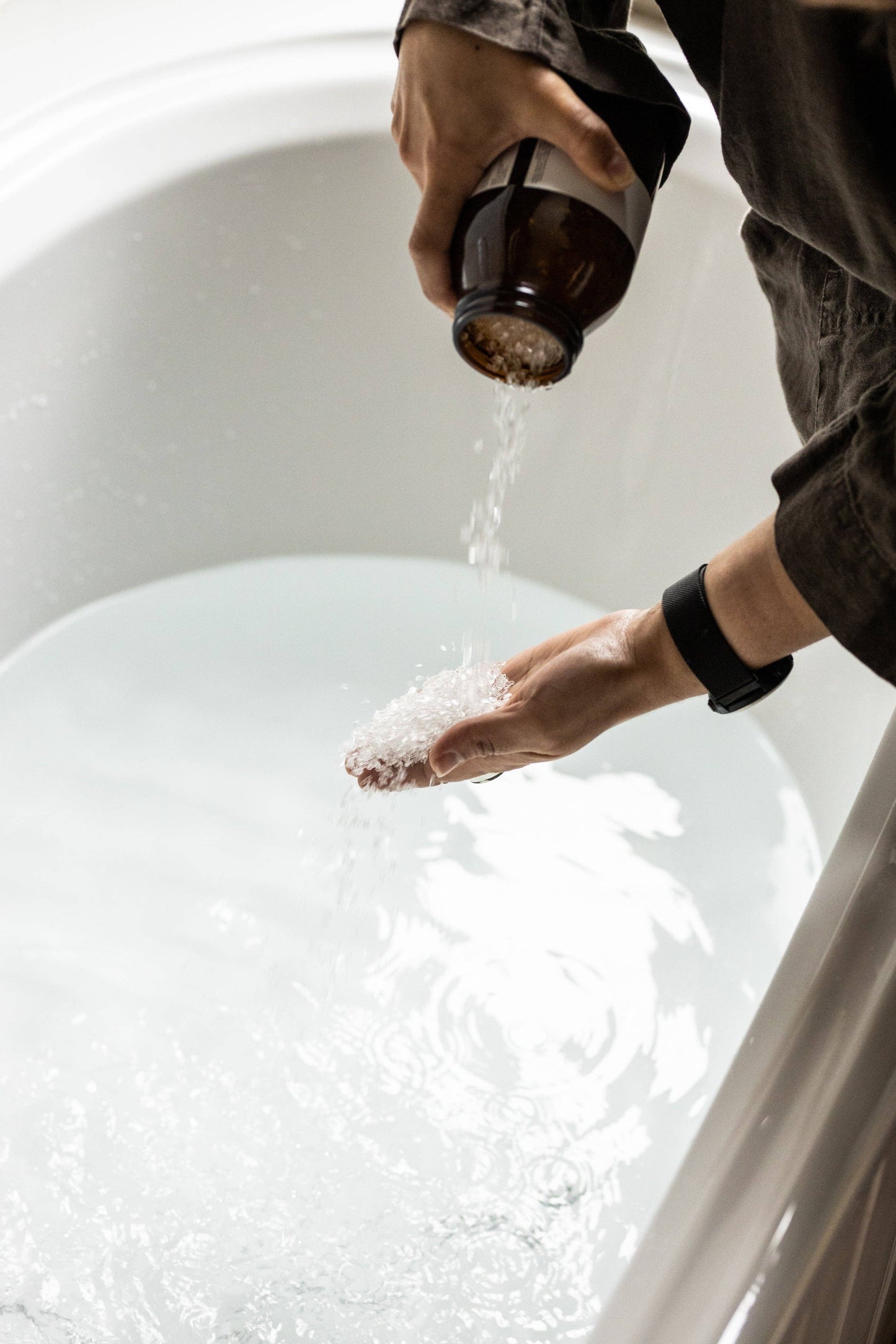 Hands pouring Harvest bathing salts from amber jar into white bath