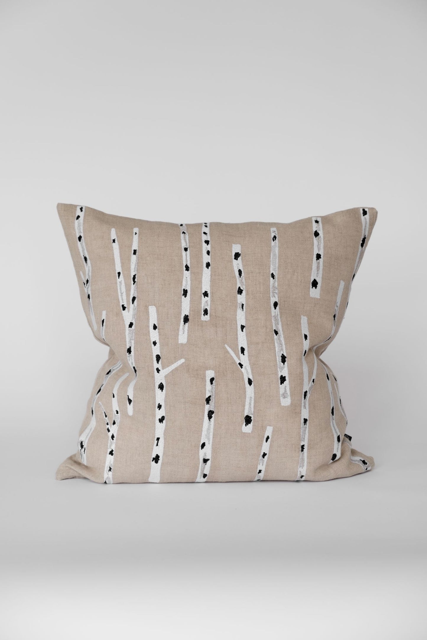 Decorative pillow with embroidered birch pattern on a plain background.