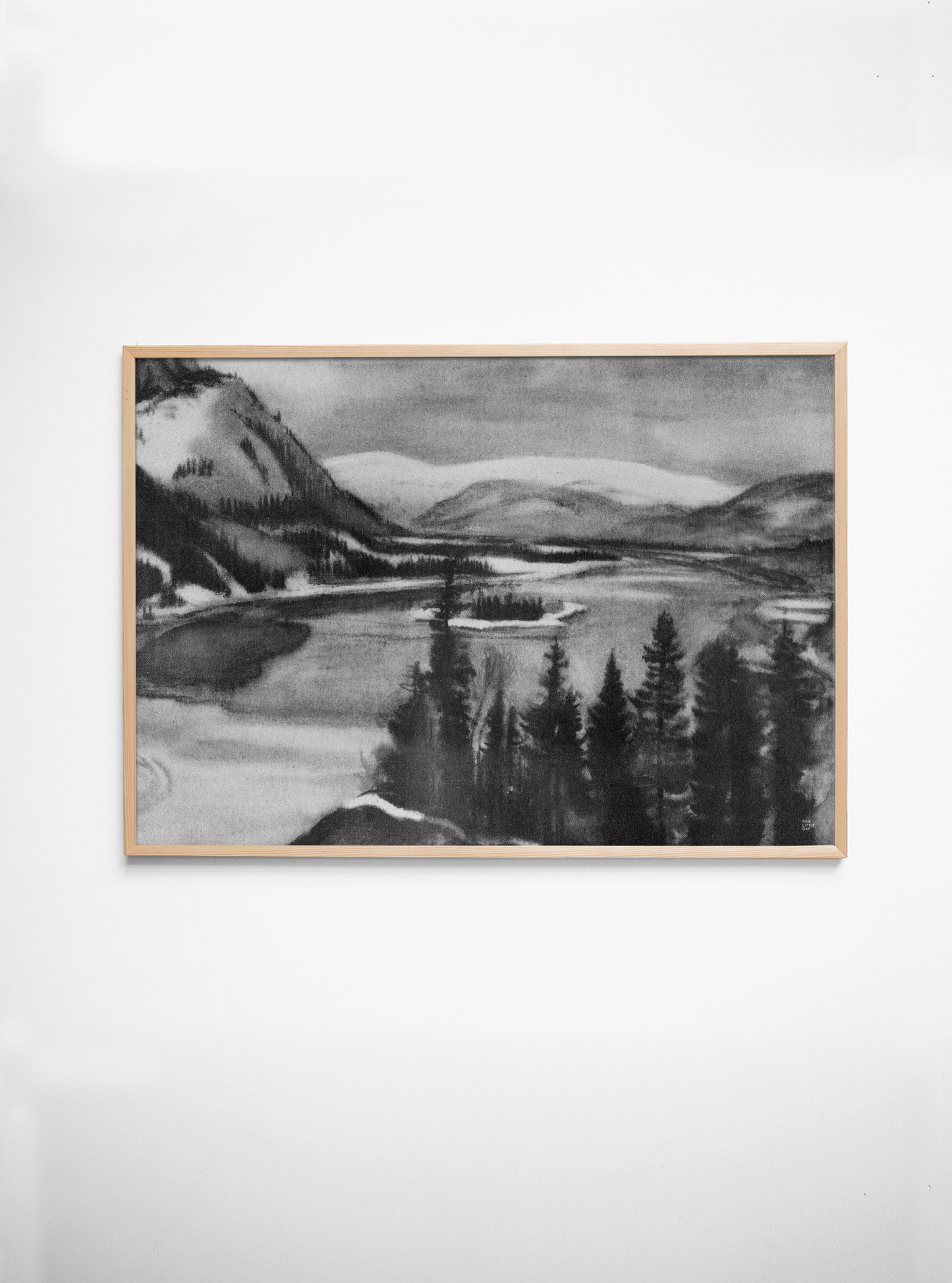 Framed black and white landscape painting of a lake and mountains on a white wall.