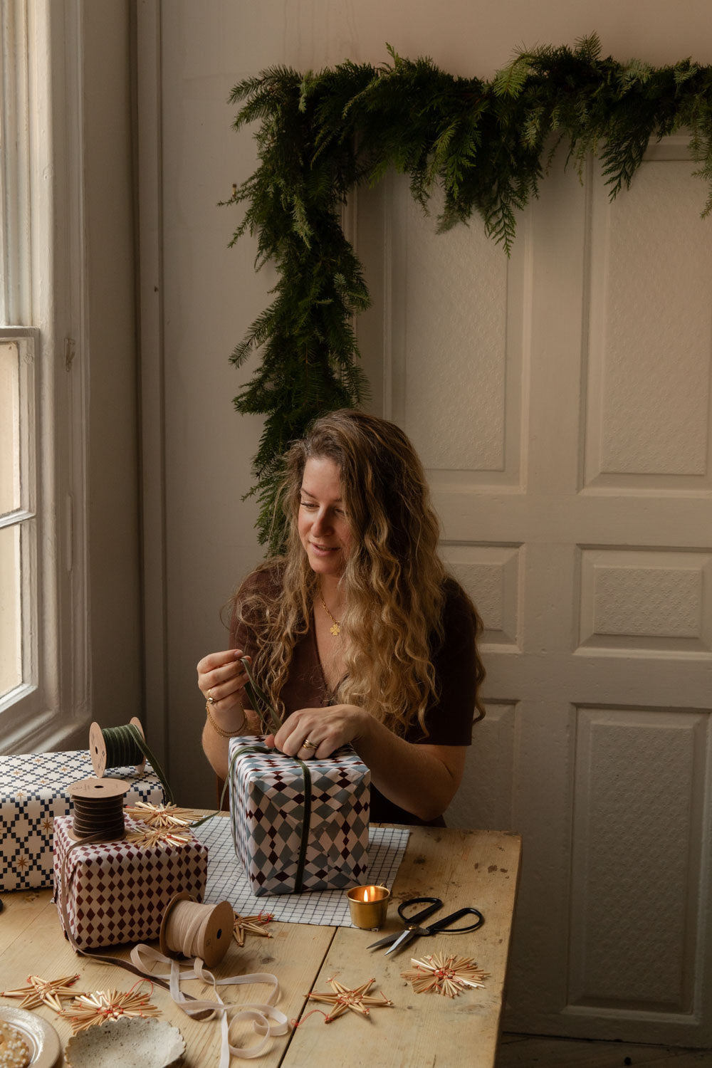Woman tying ribbon on harlequin wrapped gifts at a pine table