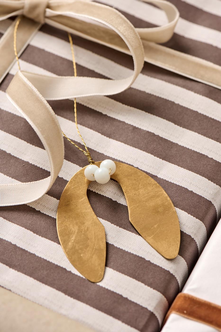 Gold leaf-shaped ornament with white beads on a striped fabric background