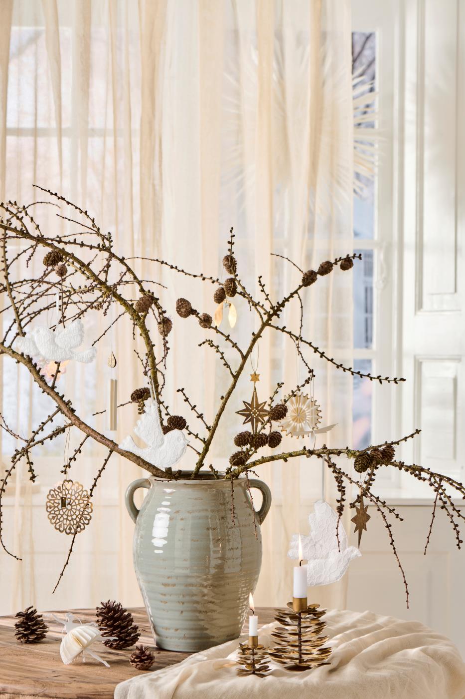 Decorative arrangement with branches, pinecones, and a vase on a table.