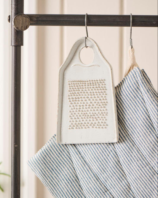 Ceramic grater and striped towel hanging on a rack with a neutral background