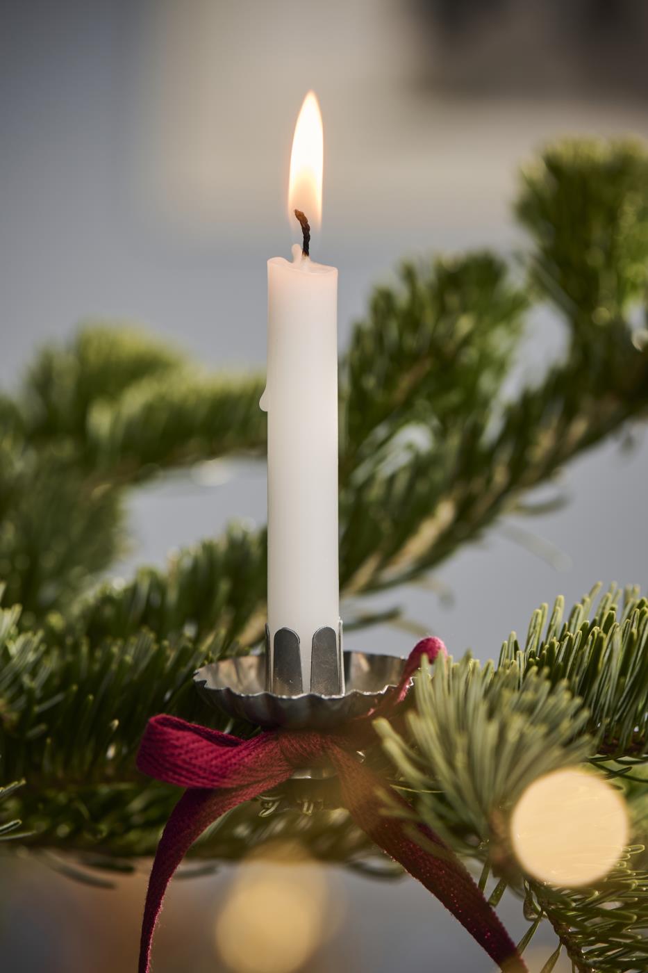 White candle in a holder on a Christmas tree branch with blurred lights in the background