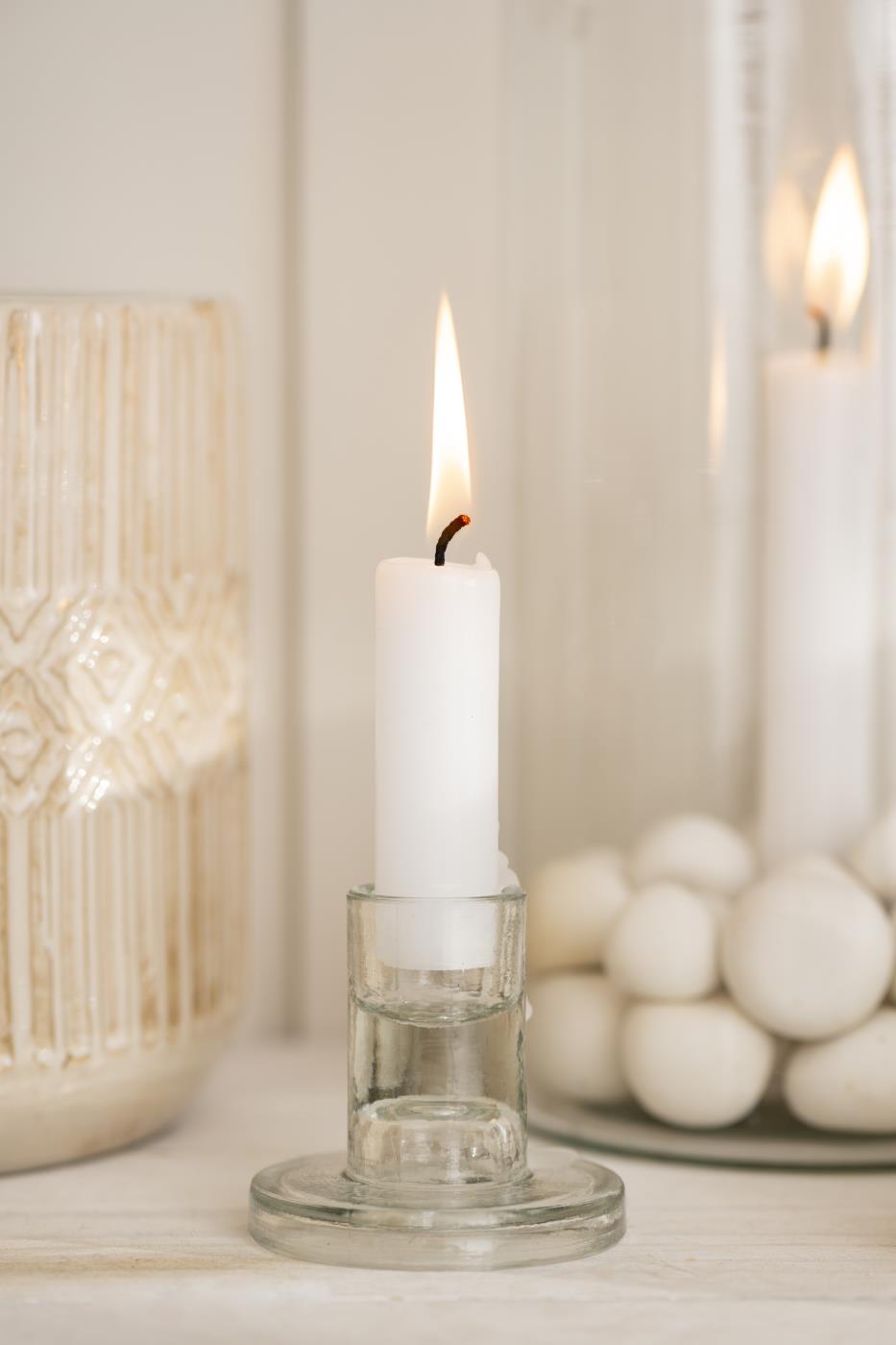 White candle in a glass holder with blurred candles and decorative items in the background