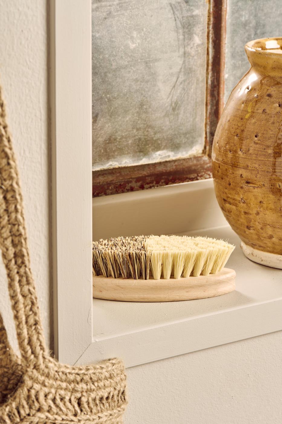 Bristle brush on a wooden stand next to a textured vase in a bathroom setting.