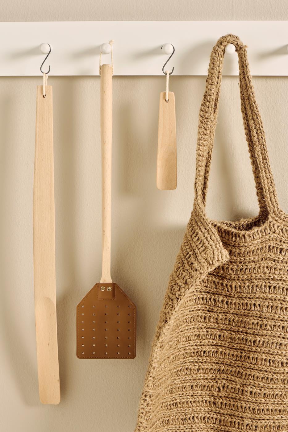 Wooden shoe horn, and woven bag hanging on a white rack against a beige wall.