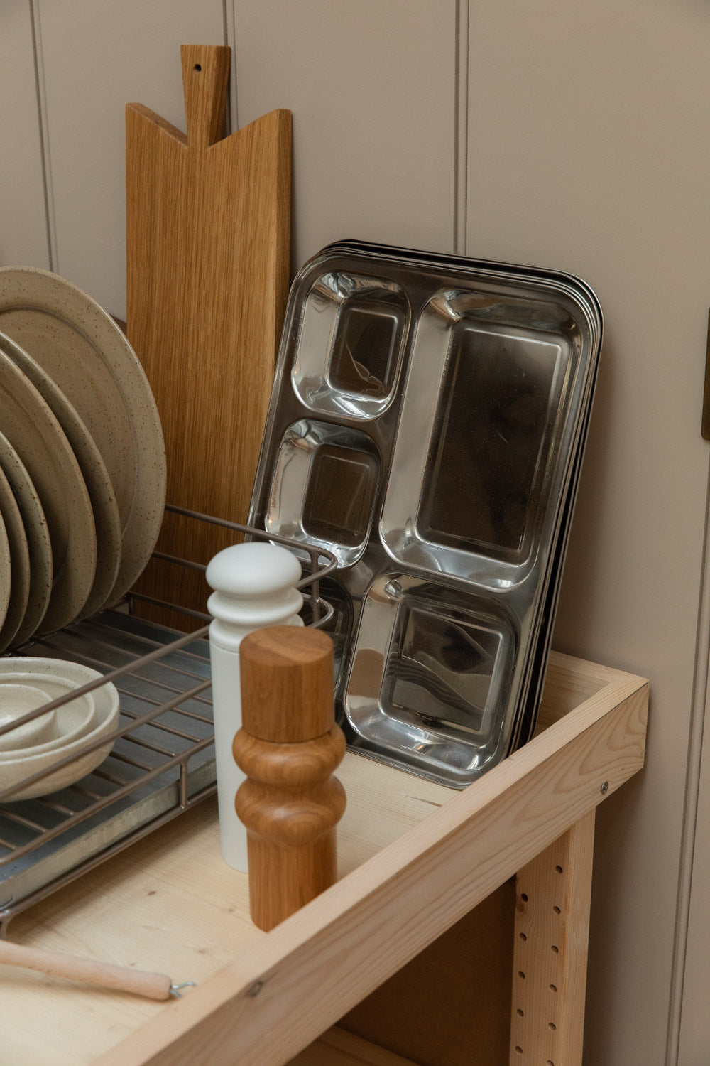 Close-up of a dish rack of stoneware plates, a stainless steel tray and a turned wooden pepper mill