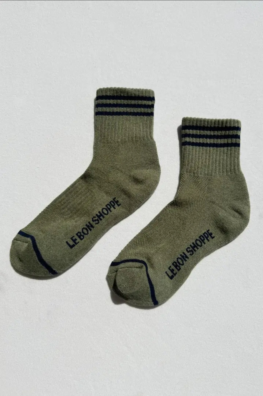 Pair of green socks with blue stripes and 'LE-BON SHOPPE' branding on the sole on a light grey background.