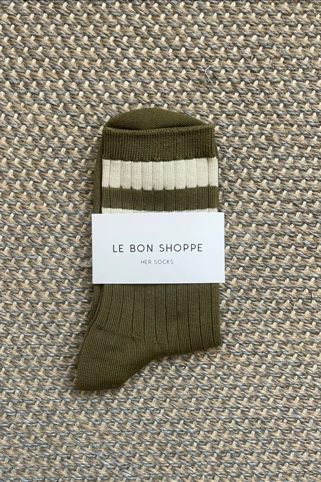 Green socks with two white stripes on textured surface.