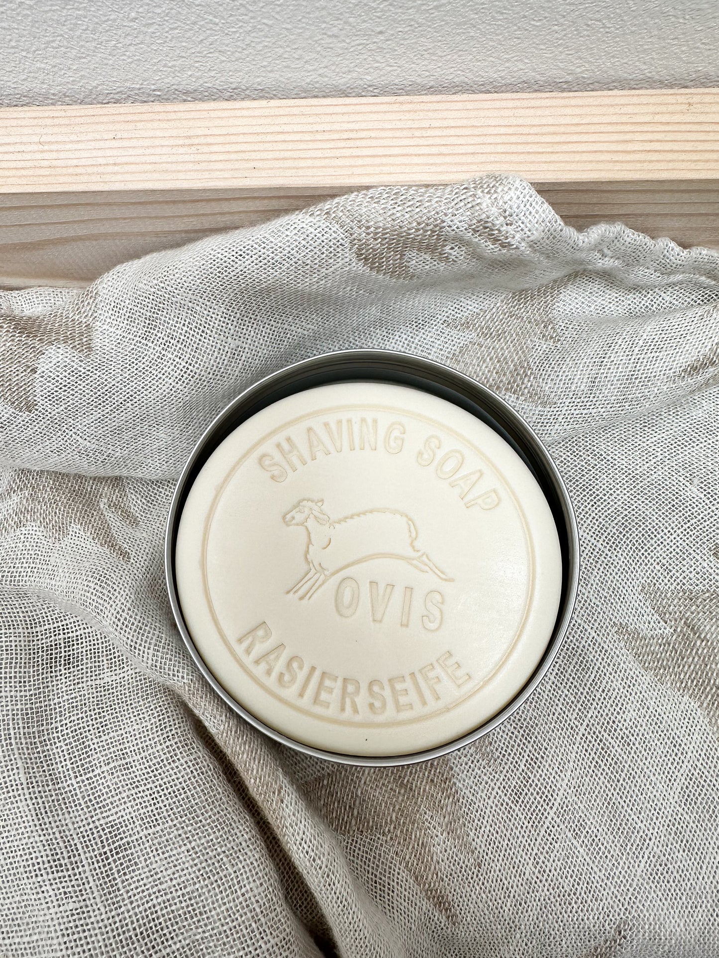 Bar of shaving soap in a tin on a textured fabric background.