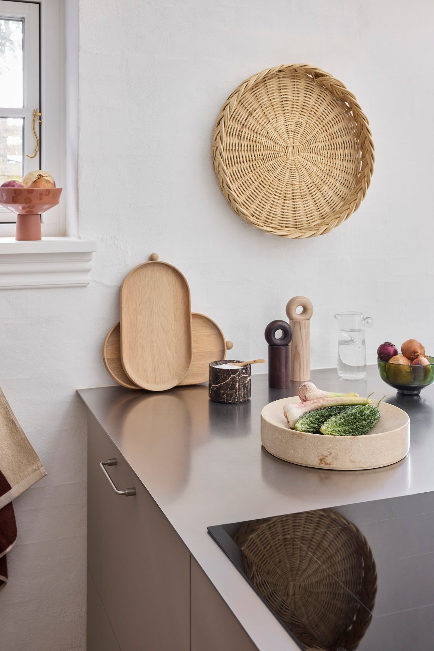 OYOY Maru Bread Basket in rattan displayed on kitchen wall above stainless steel countertop with wooden trays and kitchenware