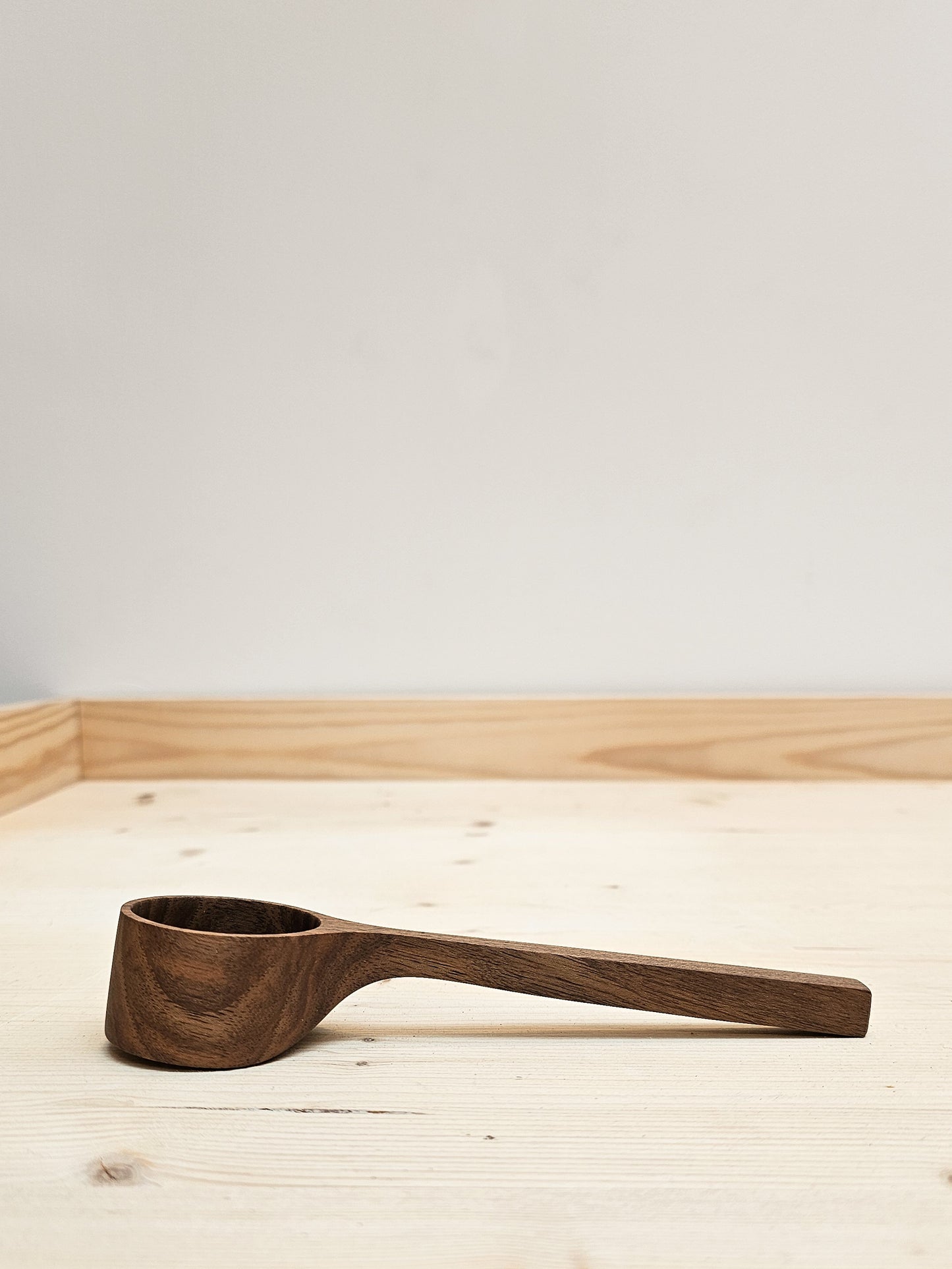 Wooden English walnut coffee scoop on a light wooden surface with a neutral background.