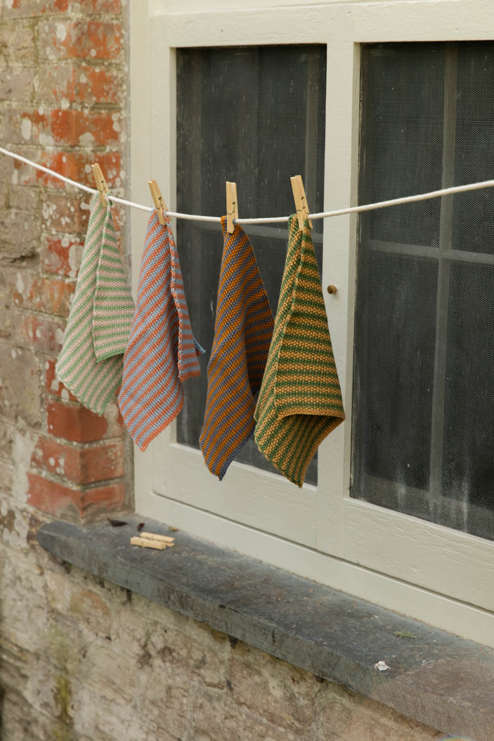 Close-up of four striped cotton dish cloths drying on a line with wooden pegs by a window