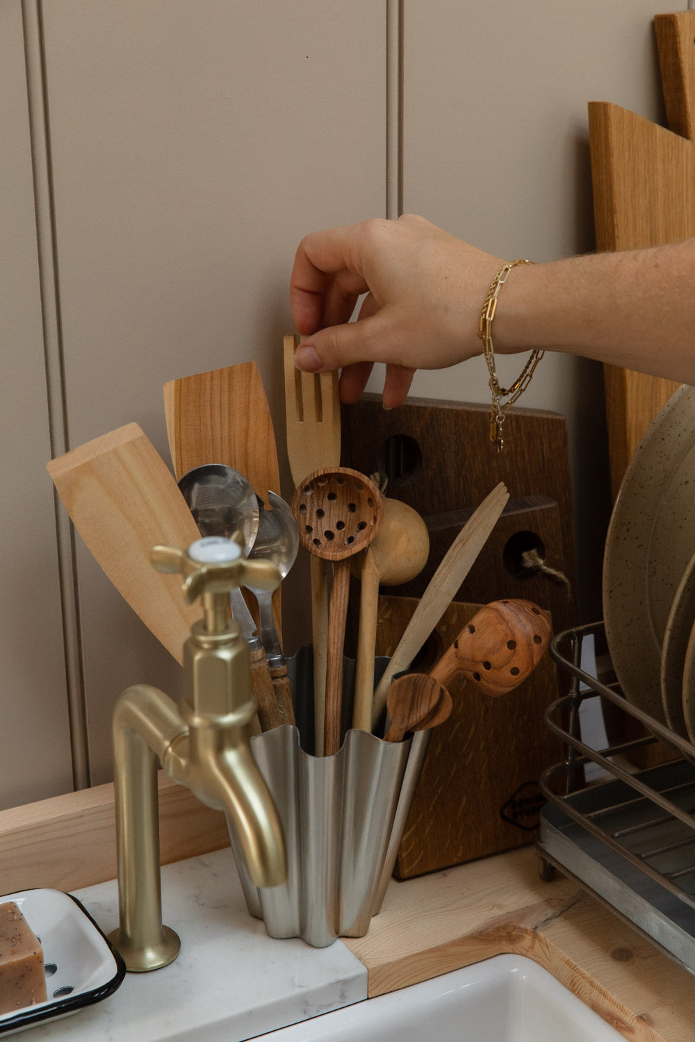 Hand selecting from a pot of wooden spoons, spatulas and slotted spoons by the sink