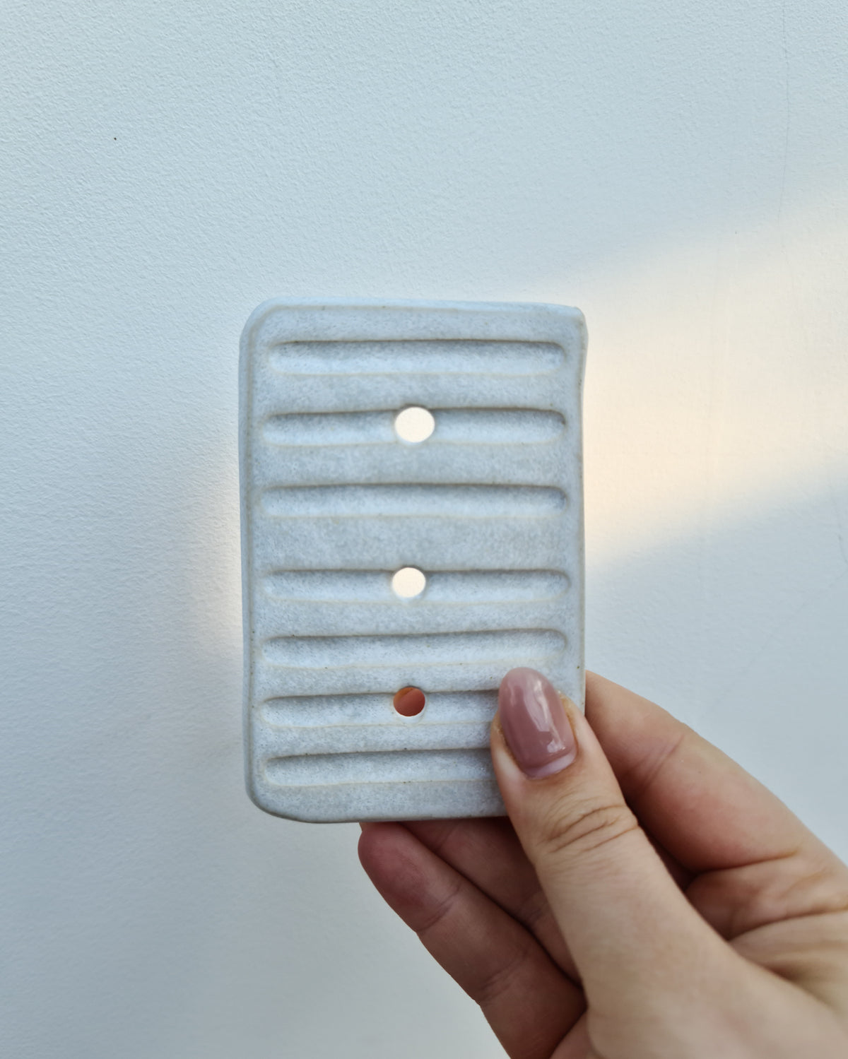 Hand holding a pale ridged ceramic soap dish with drainage holes
