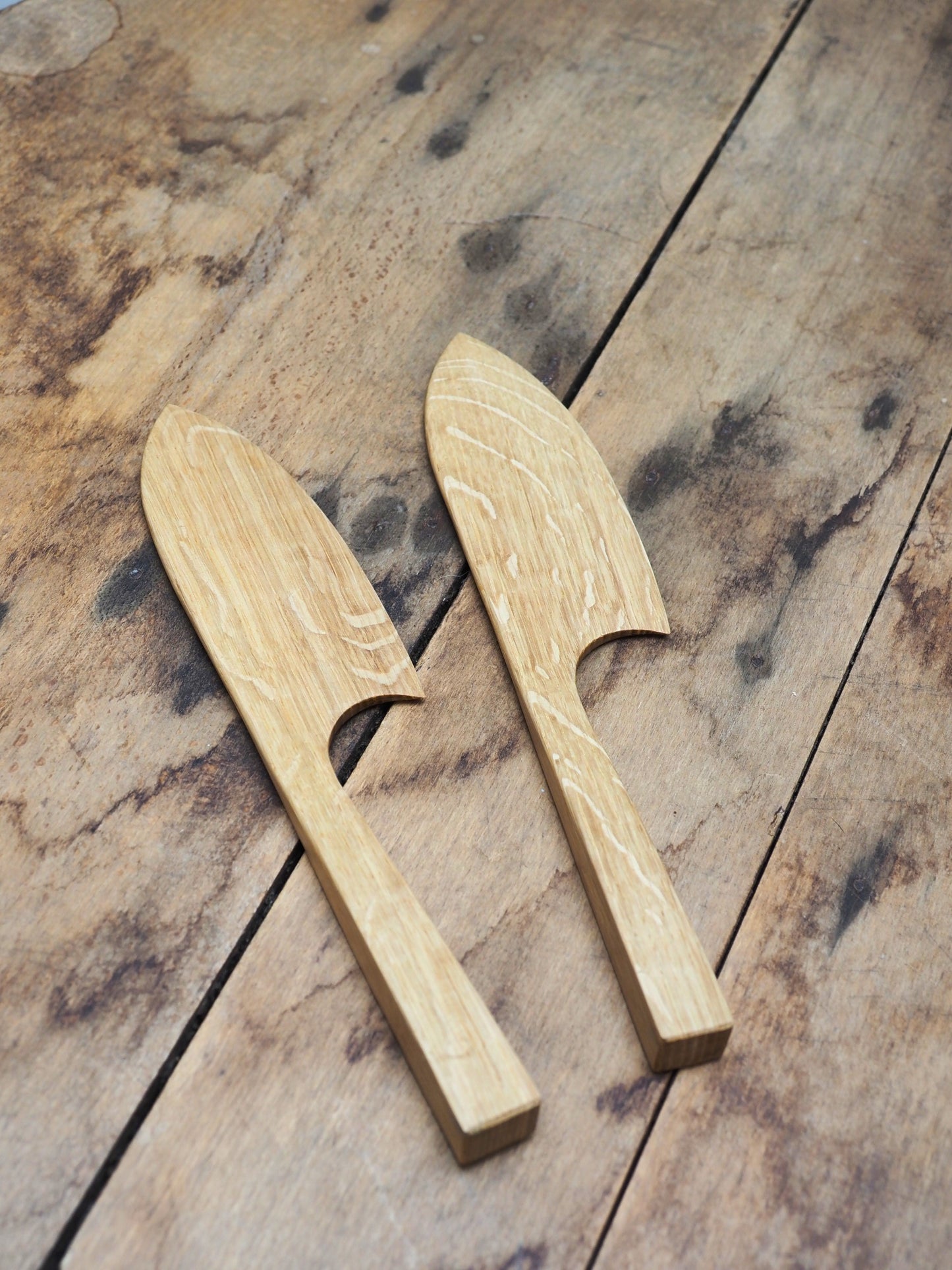 Two English Oak cake knifes laid down on a wooden table.