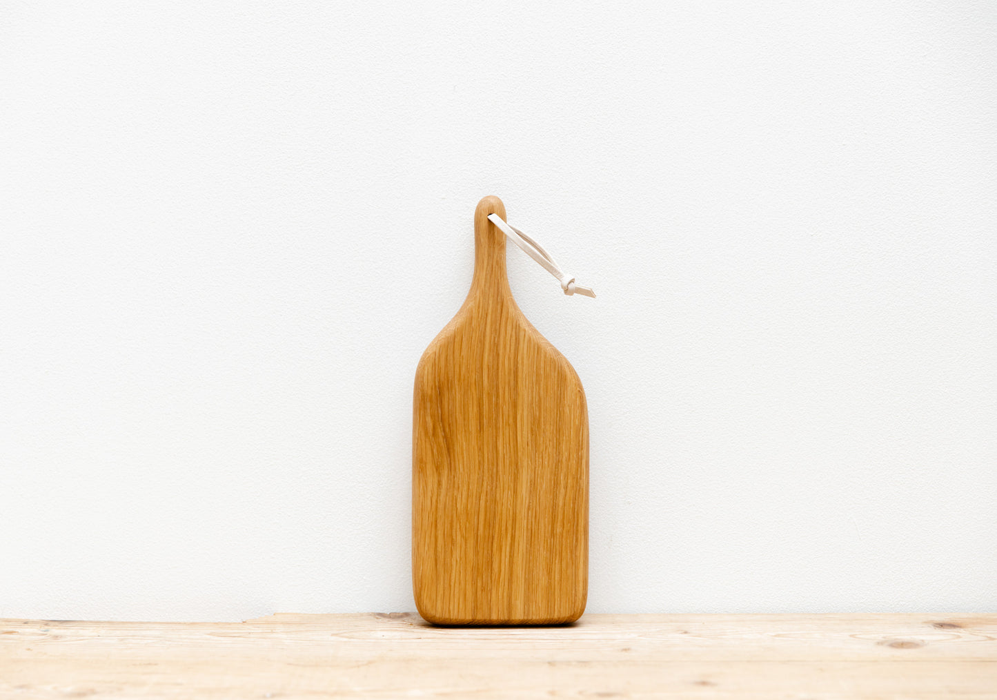 An English Oak mini board is resting up against a white background, sitting on a light wooden table top.