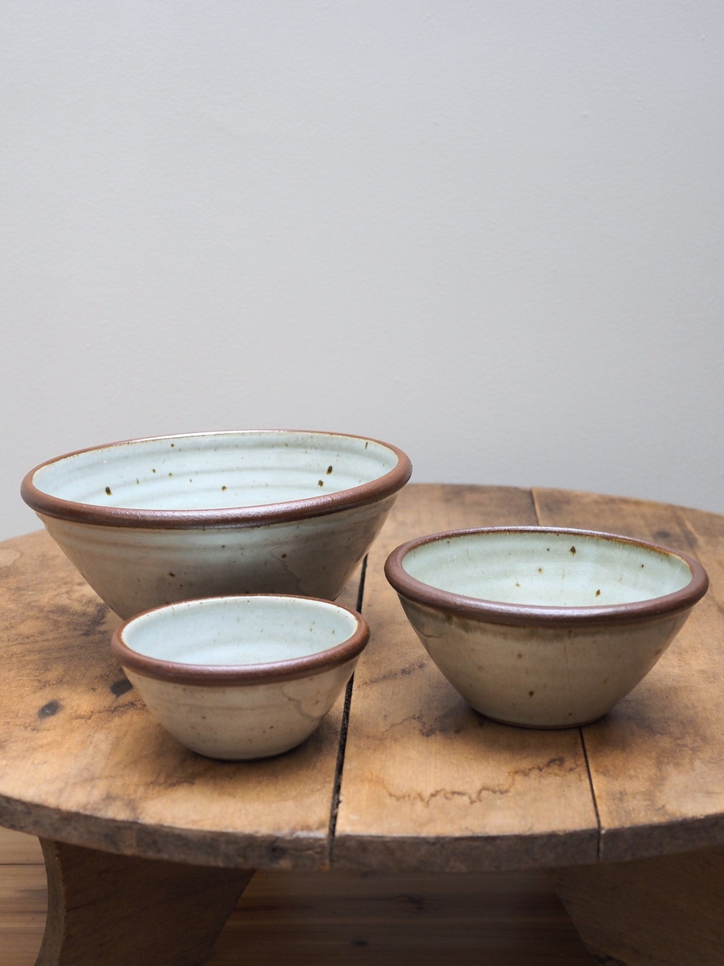 A set of three hand-thrown stoneware bowls in various sizes with a beige and brown color pattern, displayed on a wooden surface.