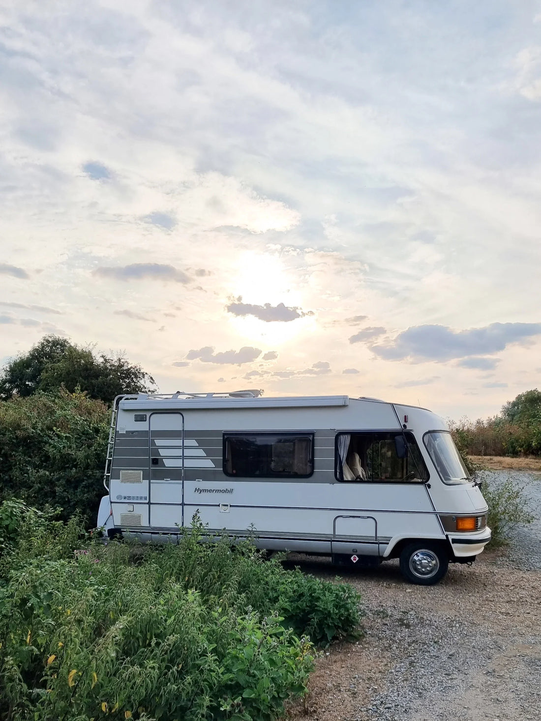 Vintage Hymermobil campervan parked amongst greenery and a beautiful sky.