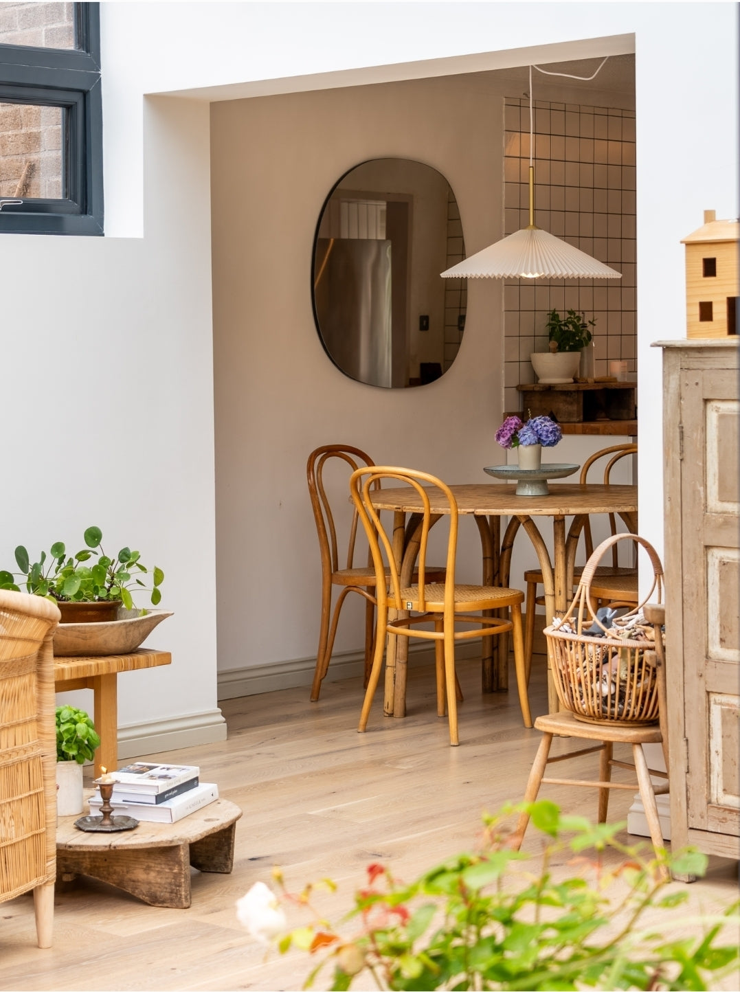 Warm, inviting dining nook with bentwood chairs and rustic wooden table, styled with fresh hydrangeas. A pleated pendant light and organic mirror add soft design details, with natural textures and plants completing the calm, Scandinavian-inspired space.