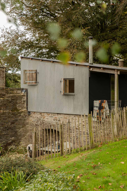 Tin-roofed cabin in an autumn garden with wool blankets airing on the veranda rail behind a chestnut paling fence