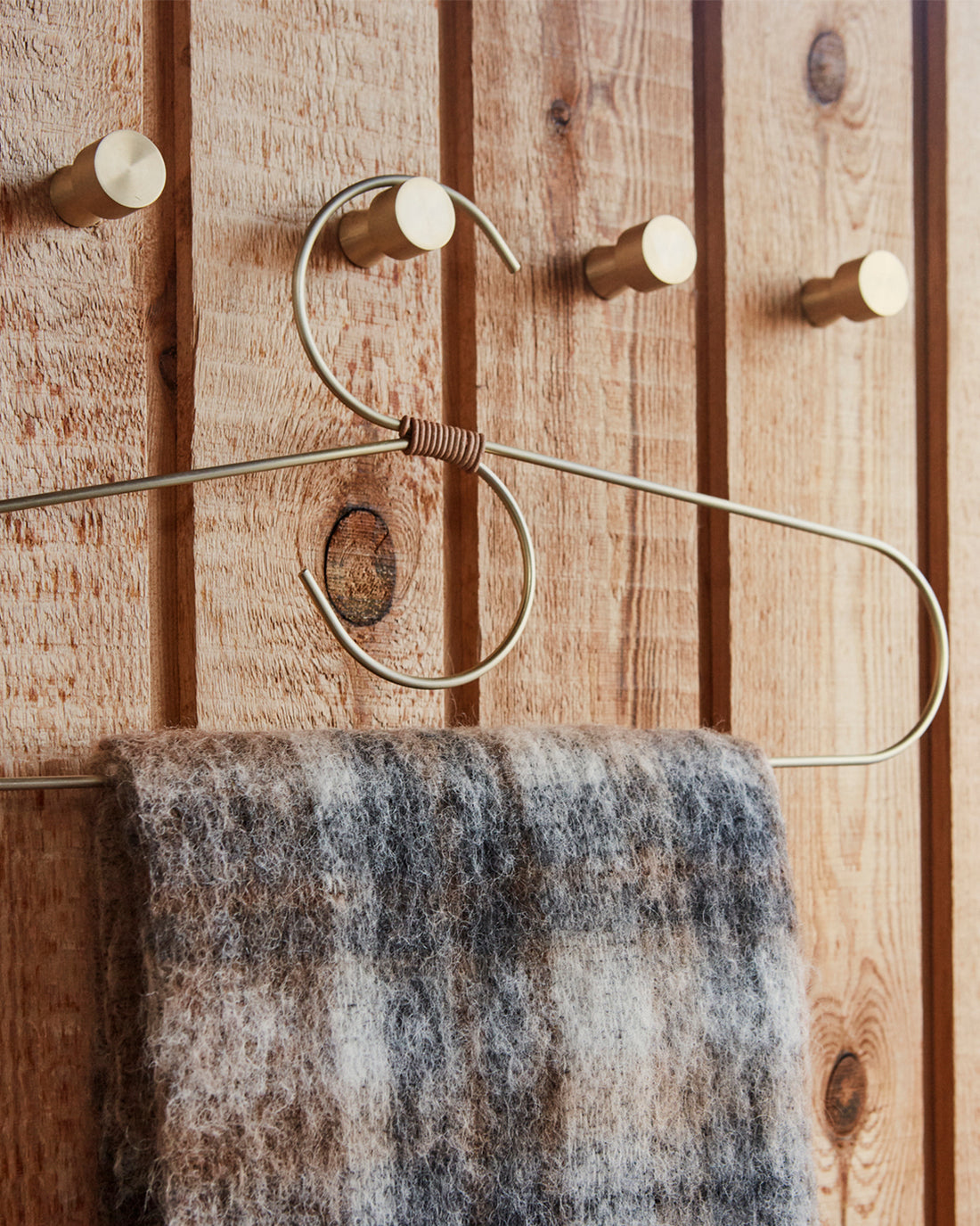 A close-up of a rustic wooden wall with a metal towel rack featuring round wooden pegs and a hanging plaid towel in gray, brown, and white.