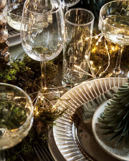 Battery powered fairy lights, strewn through a beautifully laid party table with ceramics, glassware and moss.