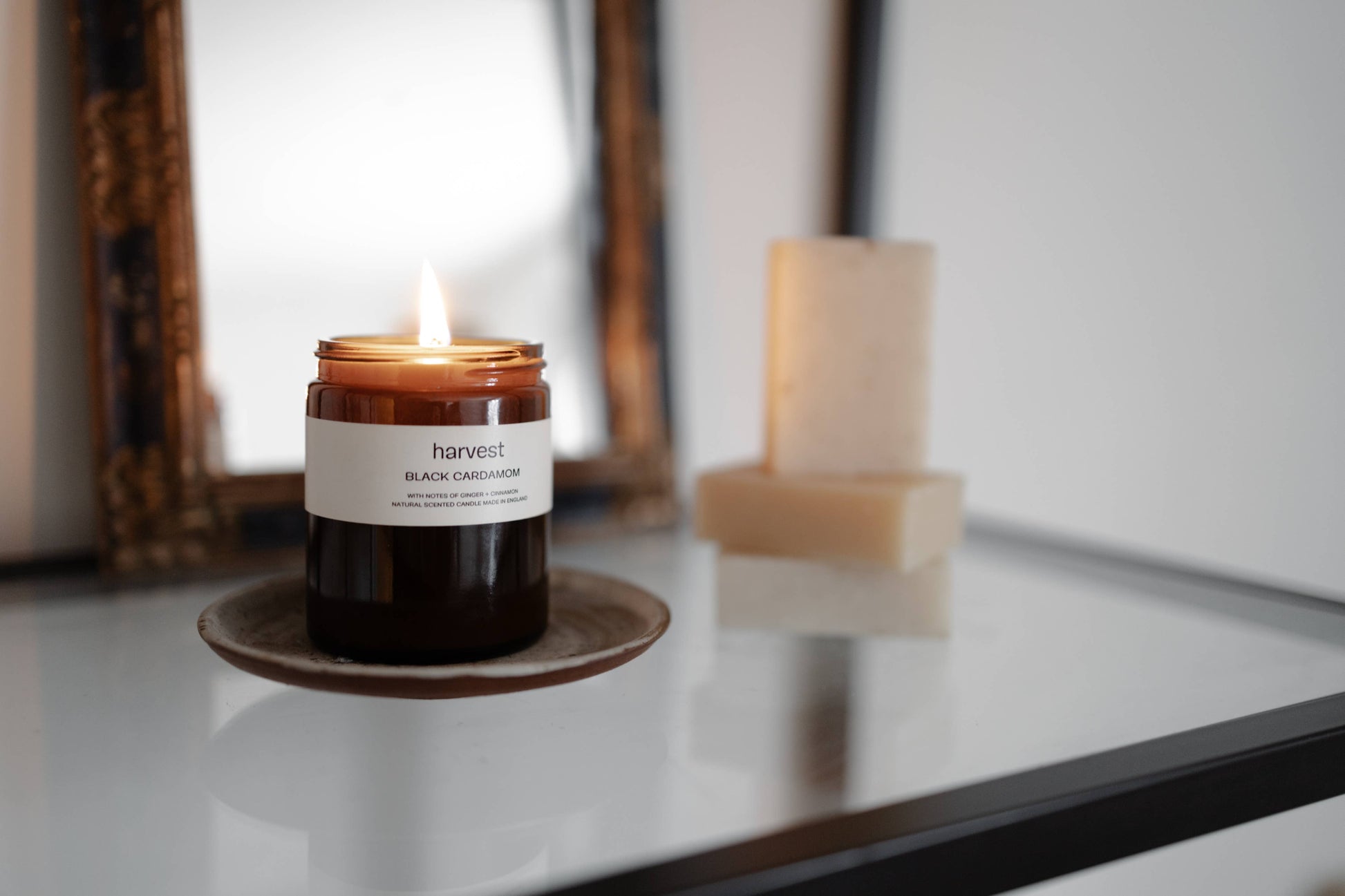 Lit Harvest Black Cardamom candle on ceramic dish beside antique mirror