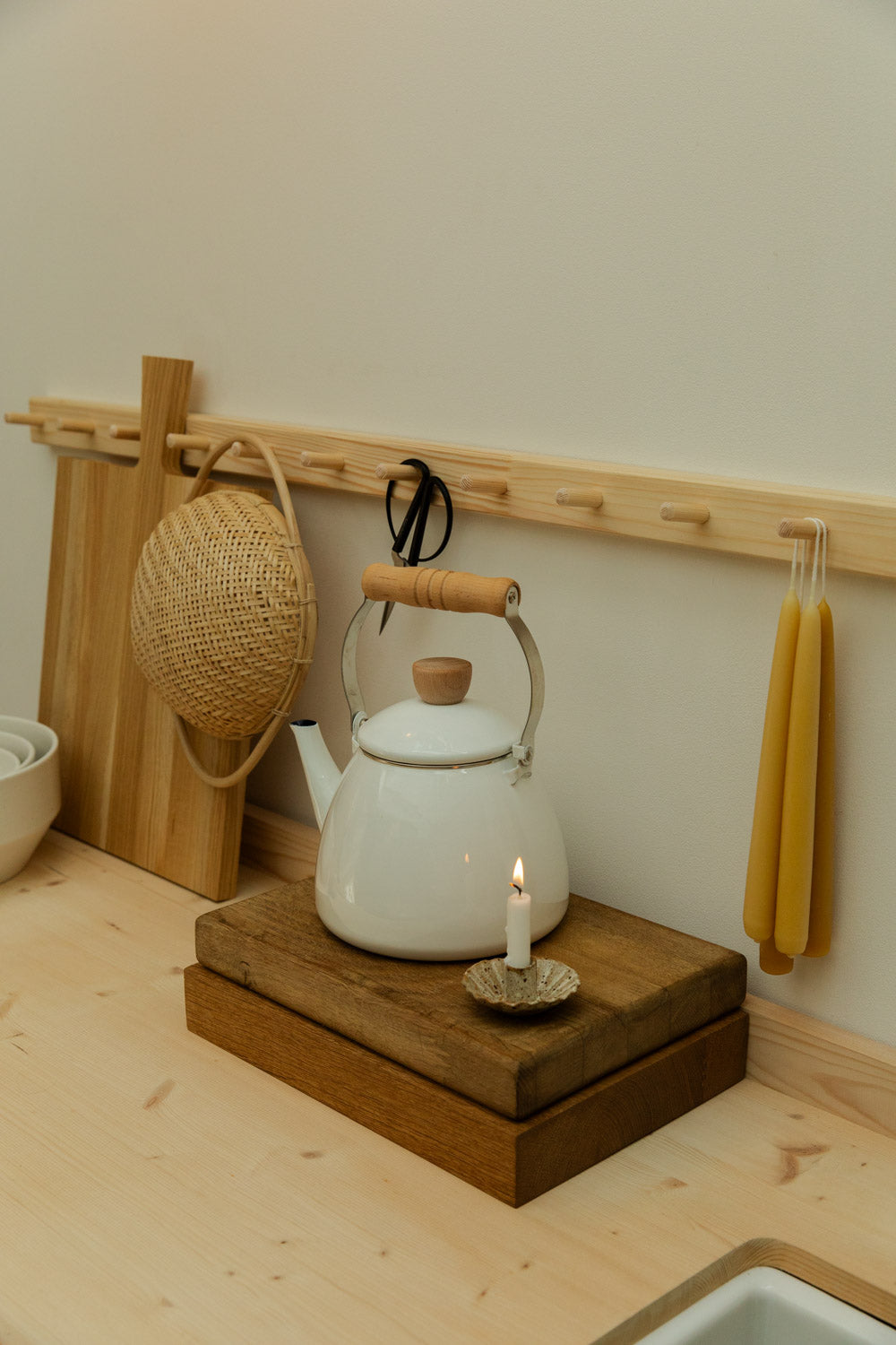 White kettle on a wooden stand with a candle, surrounded by kitchen items.