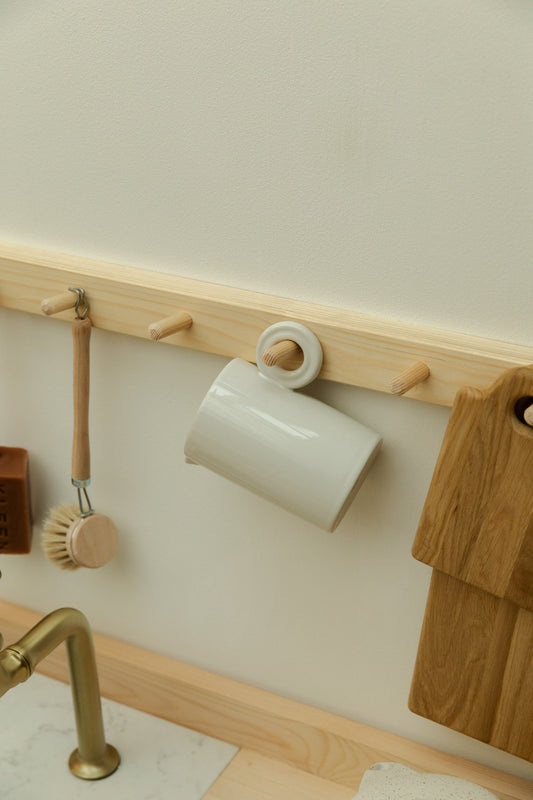 Wooden peg rail with a white jug, cleaning brush and wooden boards against a light wall.