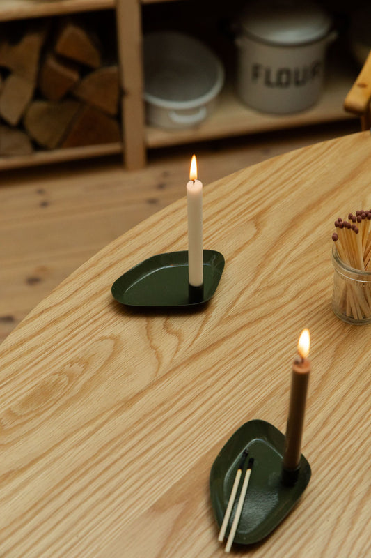 Two candle holders with lit candles on a wooden surface, with a shelf in the background.