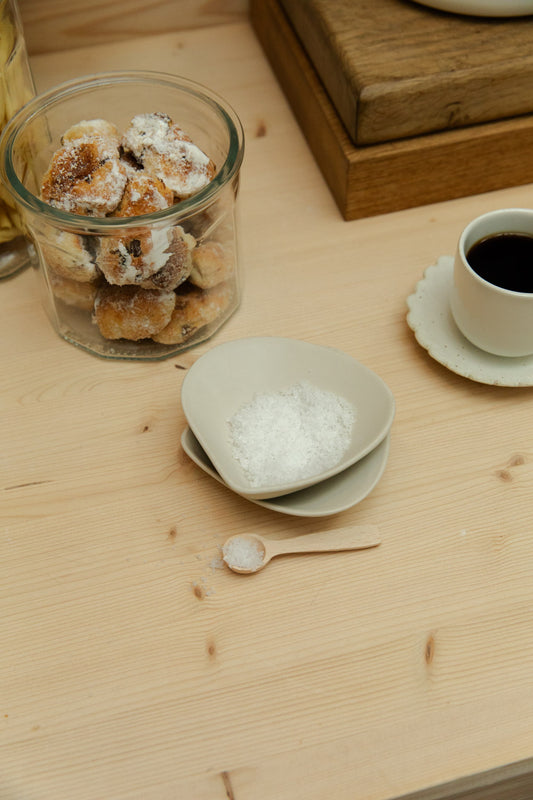Glass jar with pastries, a cup of coffee, and a small bowl on a wooden table.