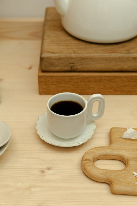 White cup of coffee on a wooden table with a teapot in the background