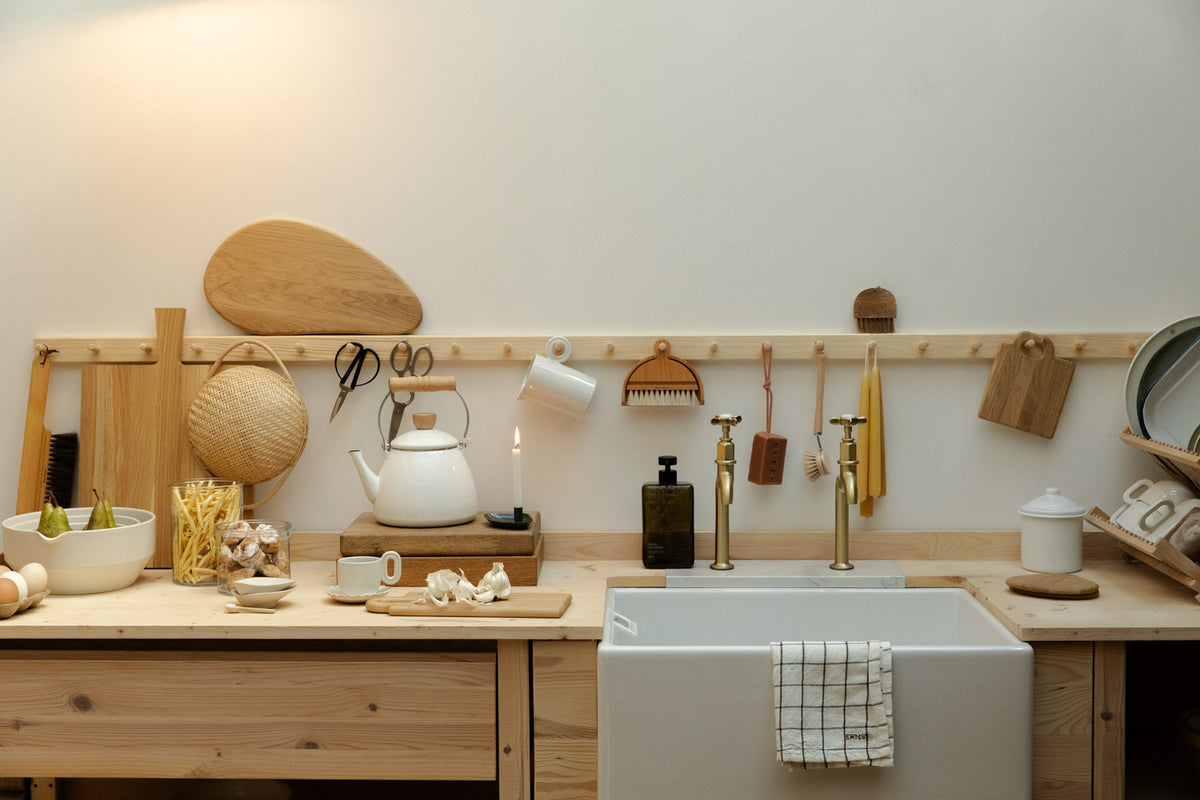Scandinavian-style kitchen with a wooden peg rail, oak chopping boards, white enamel kettle, beeswax candles and a Belfast sink with brass taps