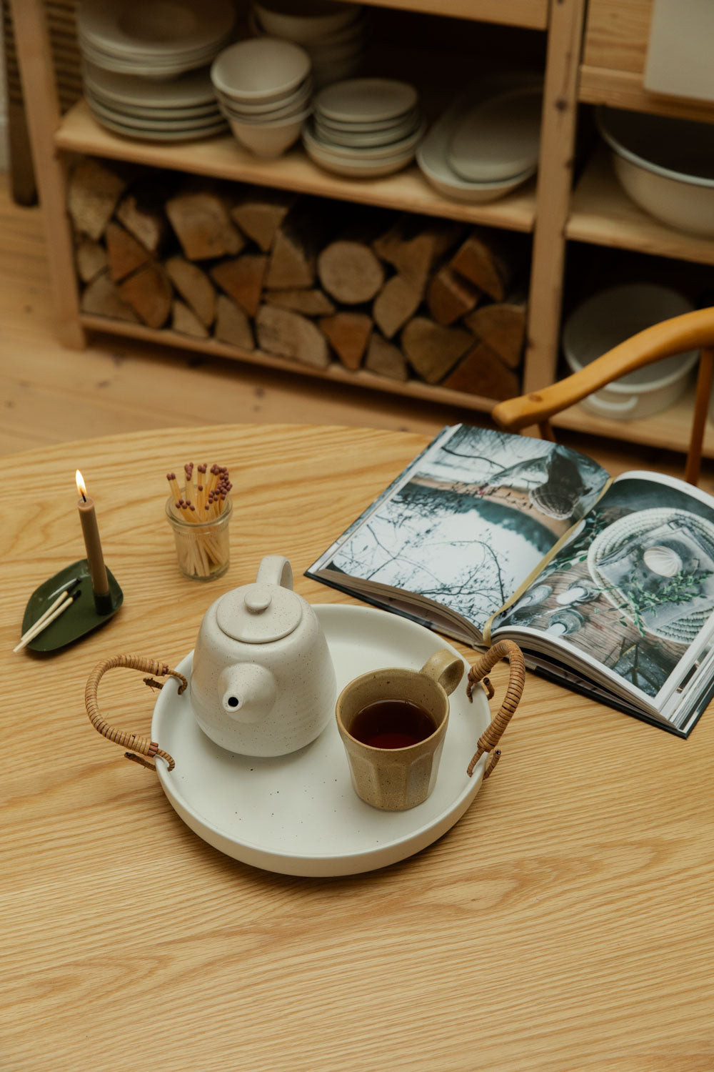 Tea set on a wooden table with a book and firewood in the background