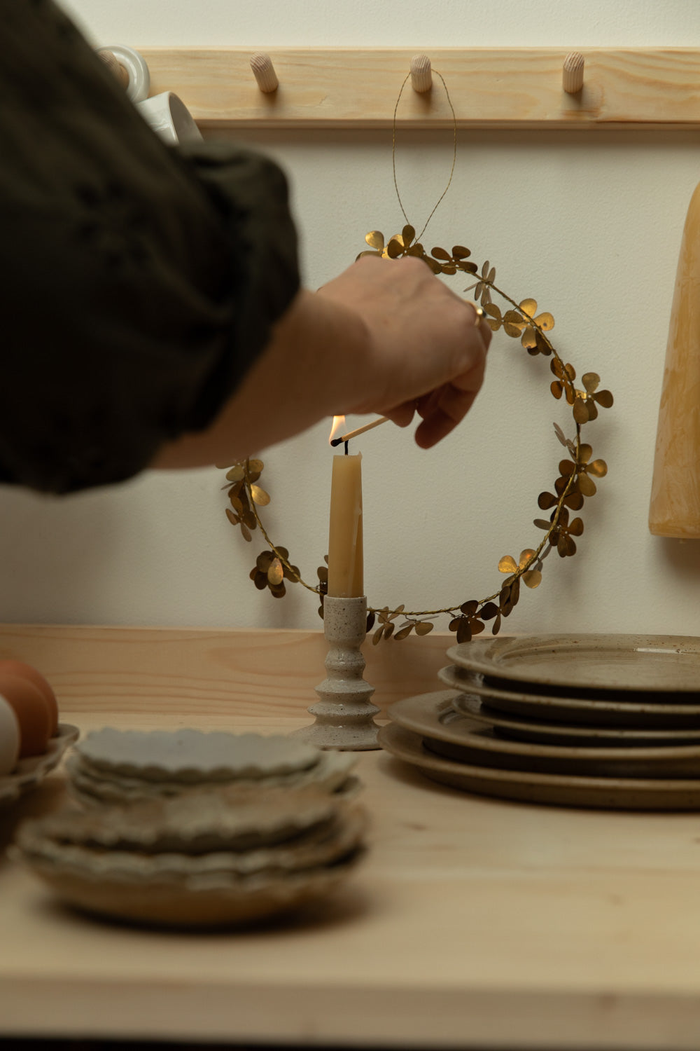 Person lighting a candle with a decorative wreath on a wooden surface