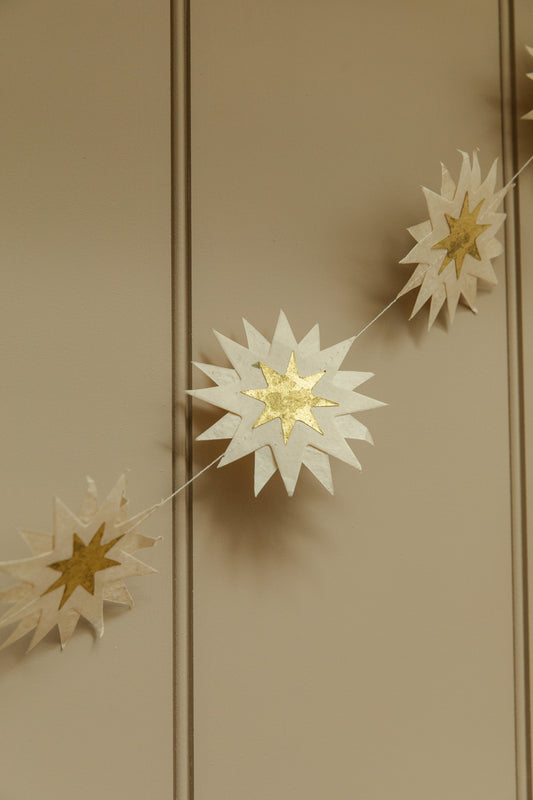 Decorative string with white and gold star-shaped ornaments on a beige wall.