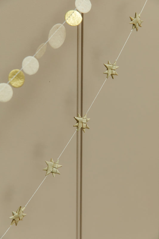 Decorative string with gold stars and circular paper garland on a beige background