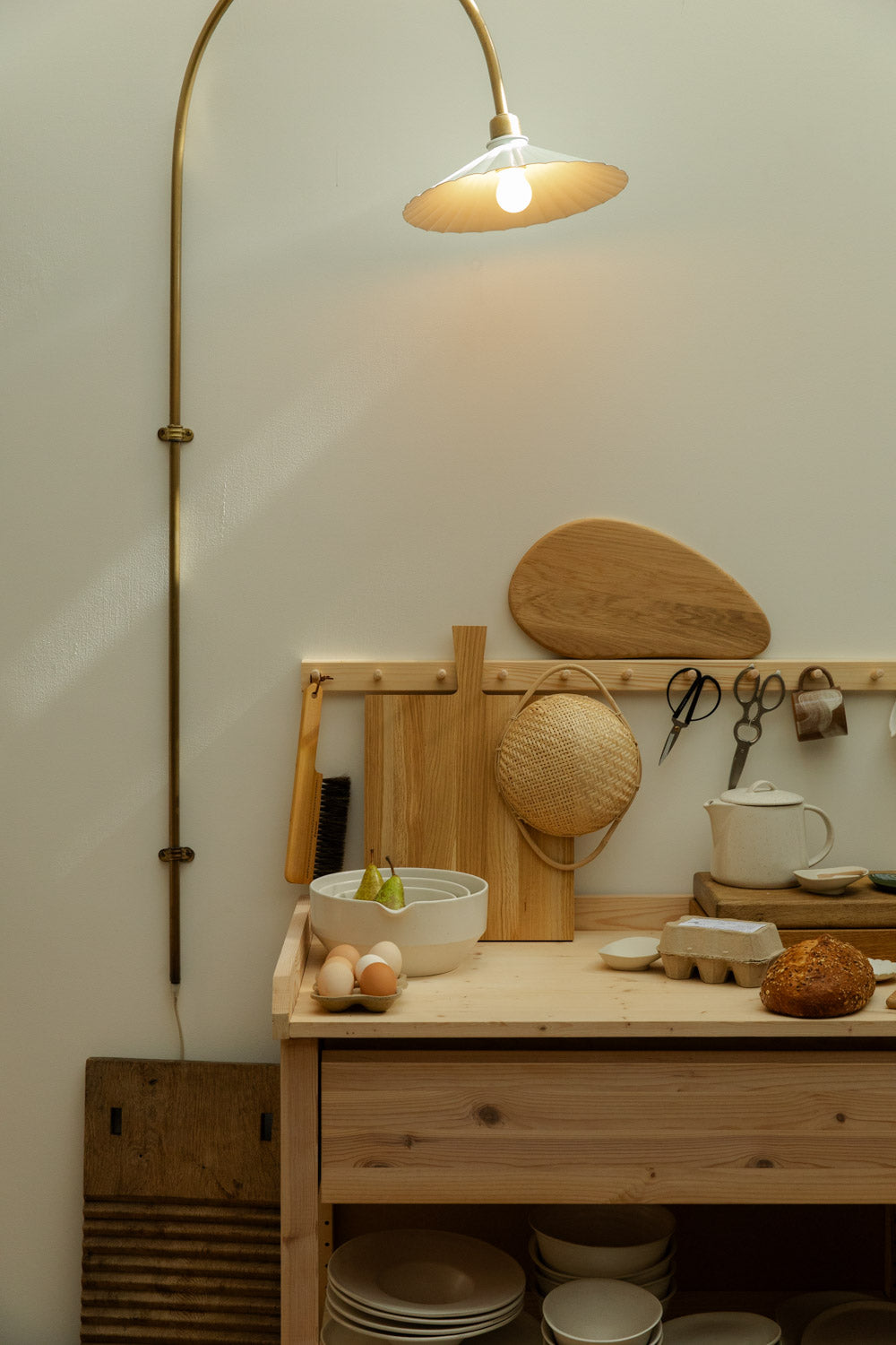Kitchen counter with wooden cutting board, bowls, and bread under a wall-mounted lamp.