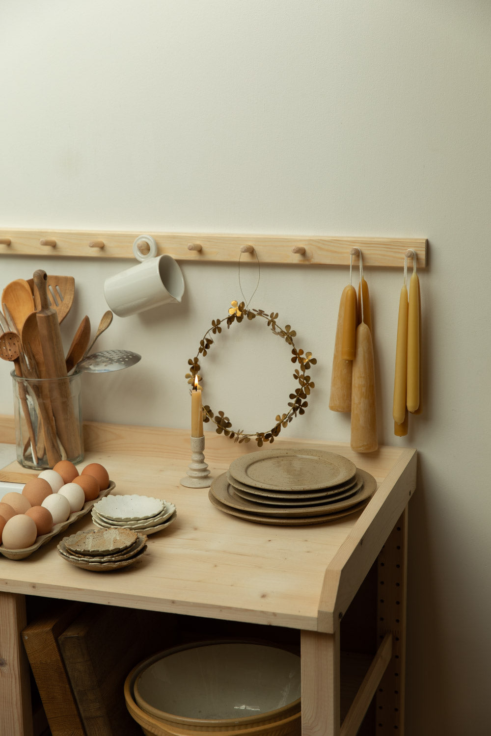 Kitchen setup with wooden table, hanging utensils, and decorative items against a light wall.