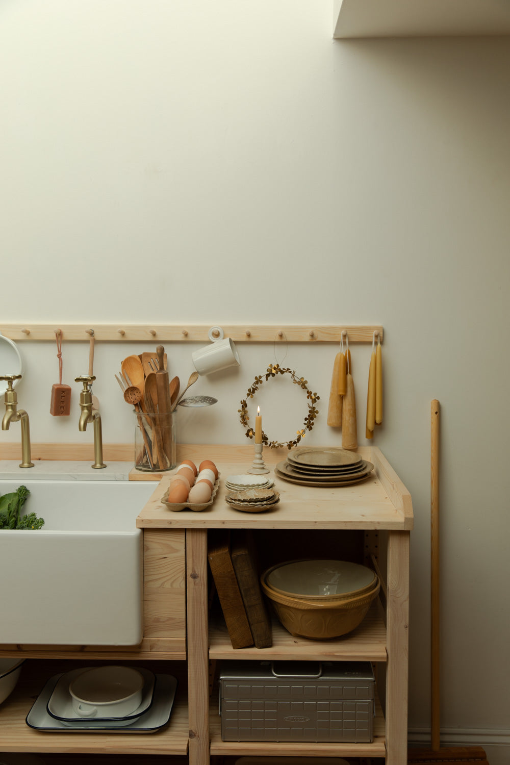 Kitchen setup with wooden counter, sink, and various kitchen items against a light wall.