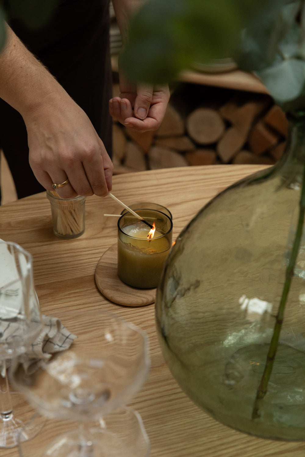 Person lighting a candle on a wooden table with a blurred background