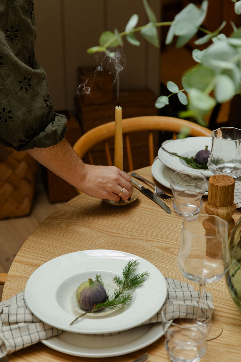 Dining table setting with plates, glasses, and a candle, with a person's hand reaching out.
