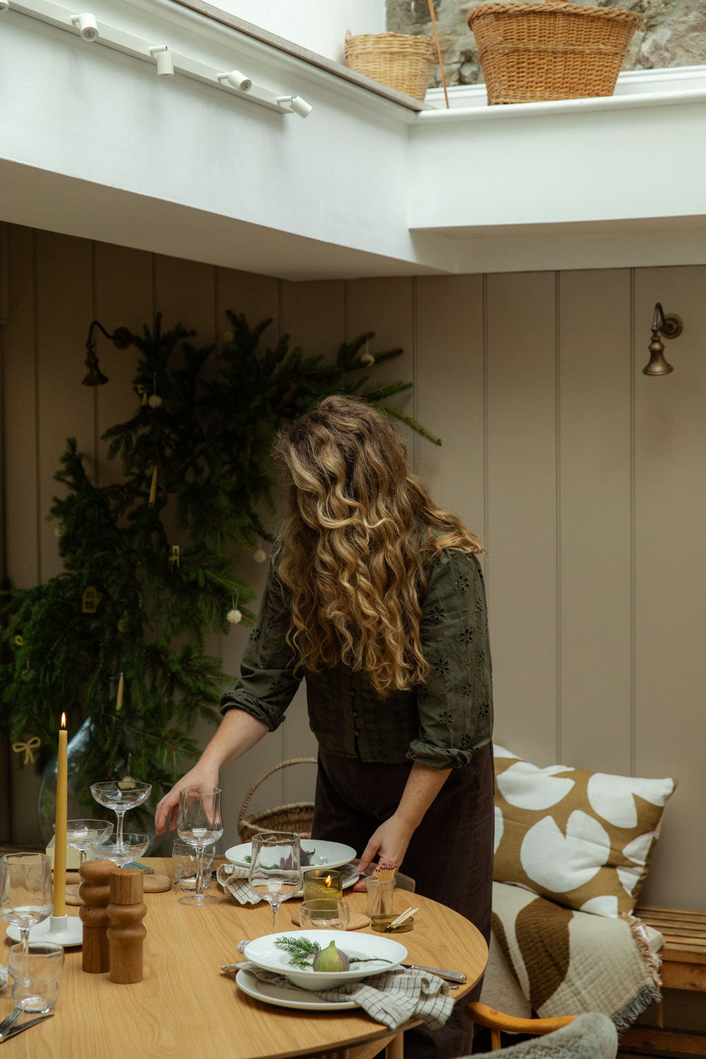 Woman setting a table in a cozy room with decorative elements.
