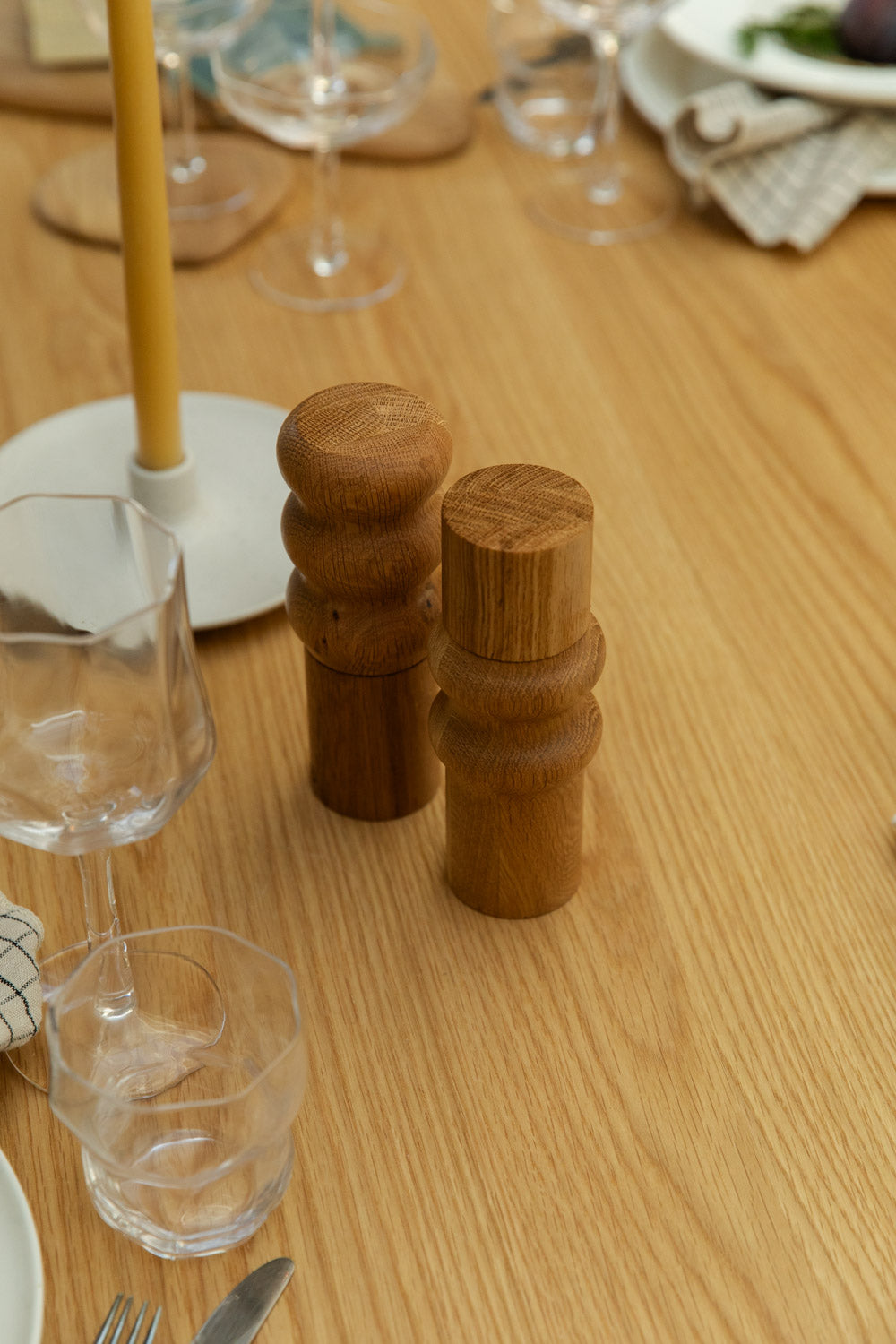 Wooden salt and pepper grinders on a wooden table with glasses and cutlery.