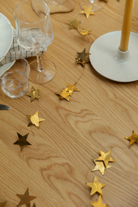 Gold star decorations on a wooden table with glasses and a candle.