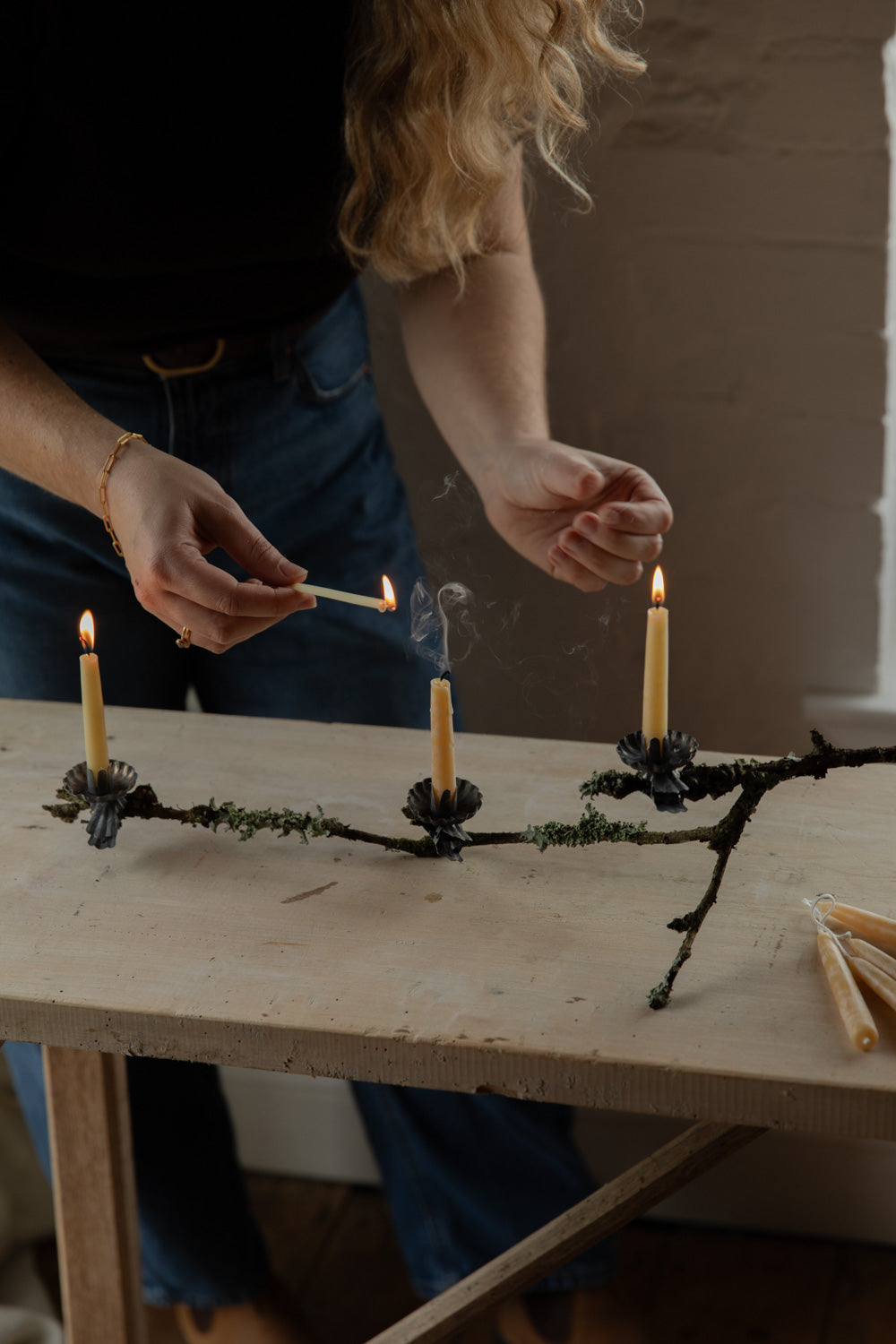 Person lighting candles on a decorative branch arrangement on a wooden table.
